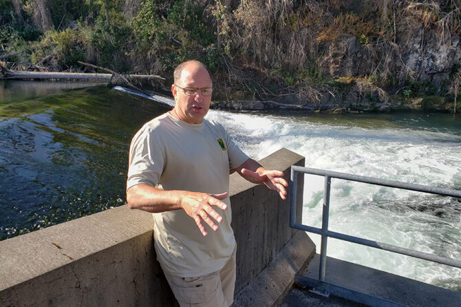 Minto fish hatchery manager Greg Grenbemer speaks in front of the water barrier in the North Santiam River that routes returning salmon into the hatchery’s fish ladders.