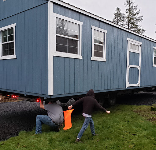 Tristan Koepl, a shed mover from Roseburg, joined by 2 of his 3 sons, works to get the new storage shed for the Canyon Crisis and Resource Center slotted into its proper place on a pad at the rear of the Crisis Center. The shed will be used to store items the Center gives away to Canyon community members. James Day